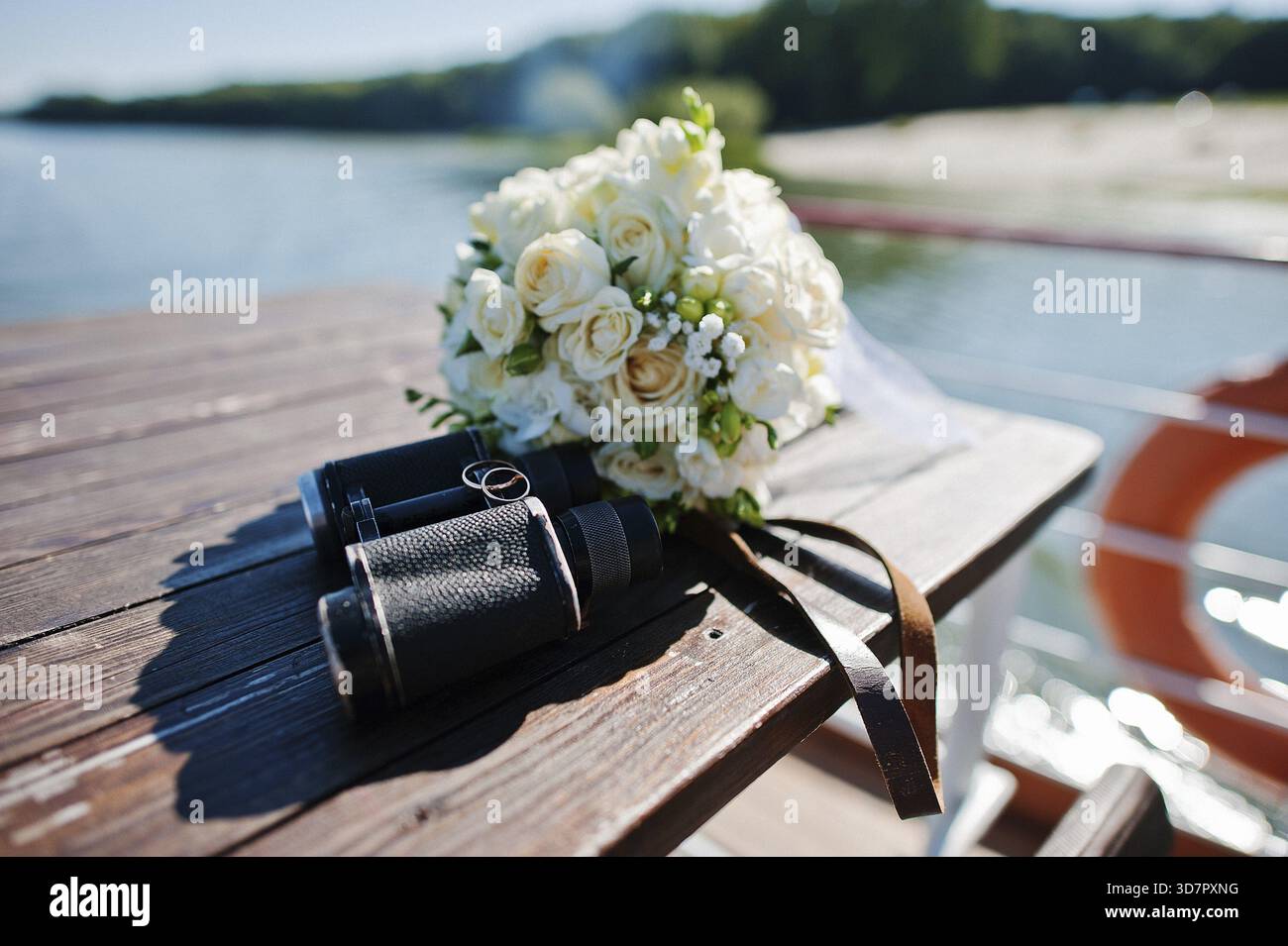 Eheringe an Ferngläsern und Blumenstrauß Stockfoto