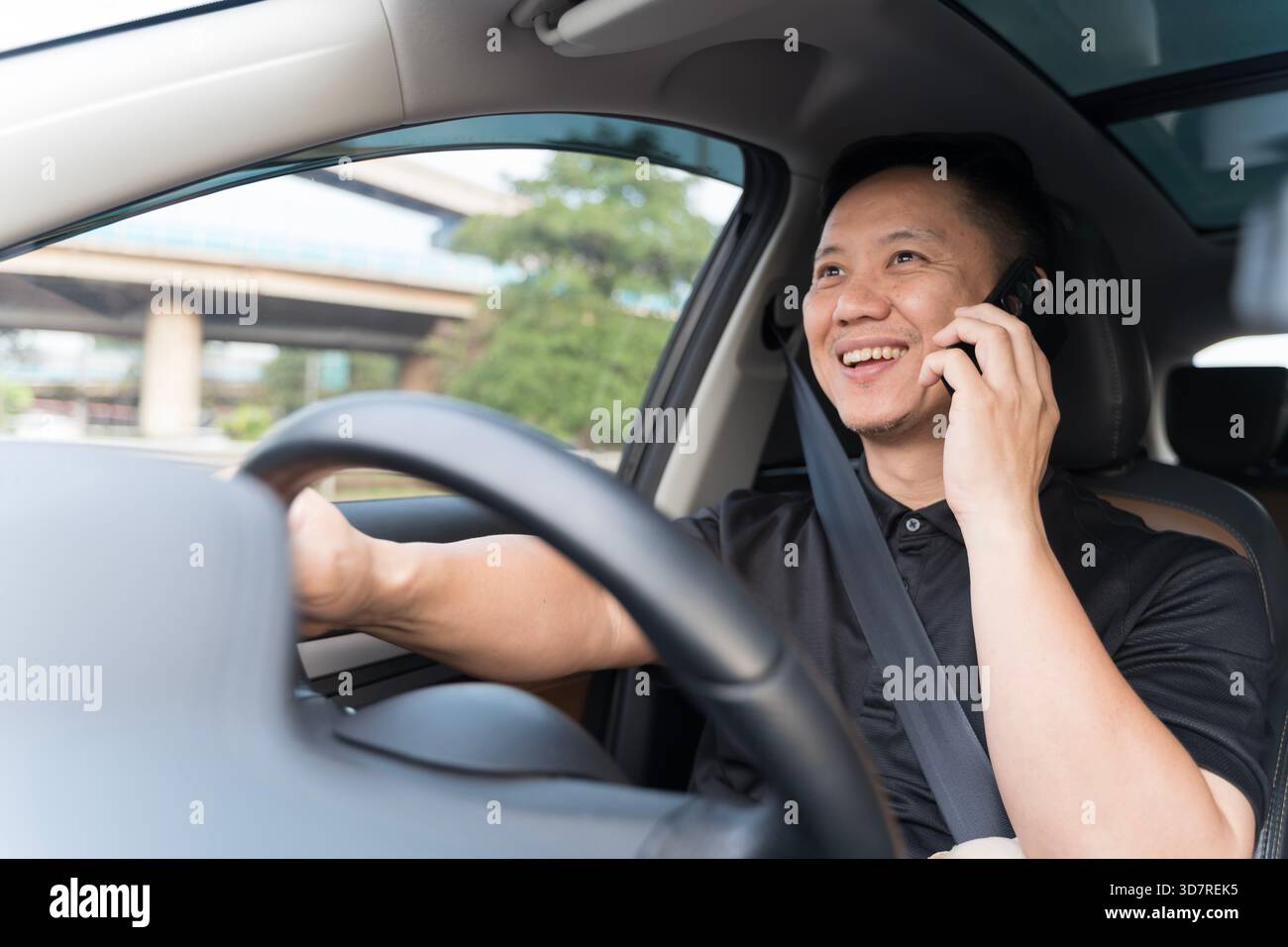 Ein Mann, der ein Auto fährt, während er mit seinem Handy spricht, zeigt abgelenktes Fahrverhalten in einem modernen Fahrzeuginnenraum, Bedenken bezüglich der Straßenverkehrssicherheit, Eve Stockfoto