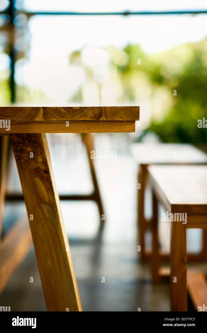 Nahaufnahme einer rustikalen Holztischkante und einem stabilen Bein, das natürliche Maserung und Handwerkskunst zeigt. Heller, unscharfer Hintergrund im Freien mit Grün. Stockfoto