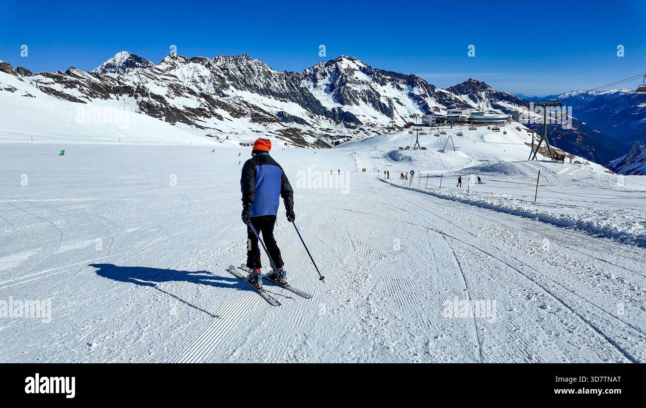 Skifahrer, der die Skipiste auf dem Stubaier Gletscher in den österreichischen Alpen hinunterläuft. Skipisten, Skifahrer und Snowboarder. Sessellift rechts, Seilbahnstation, Stockfoto