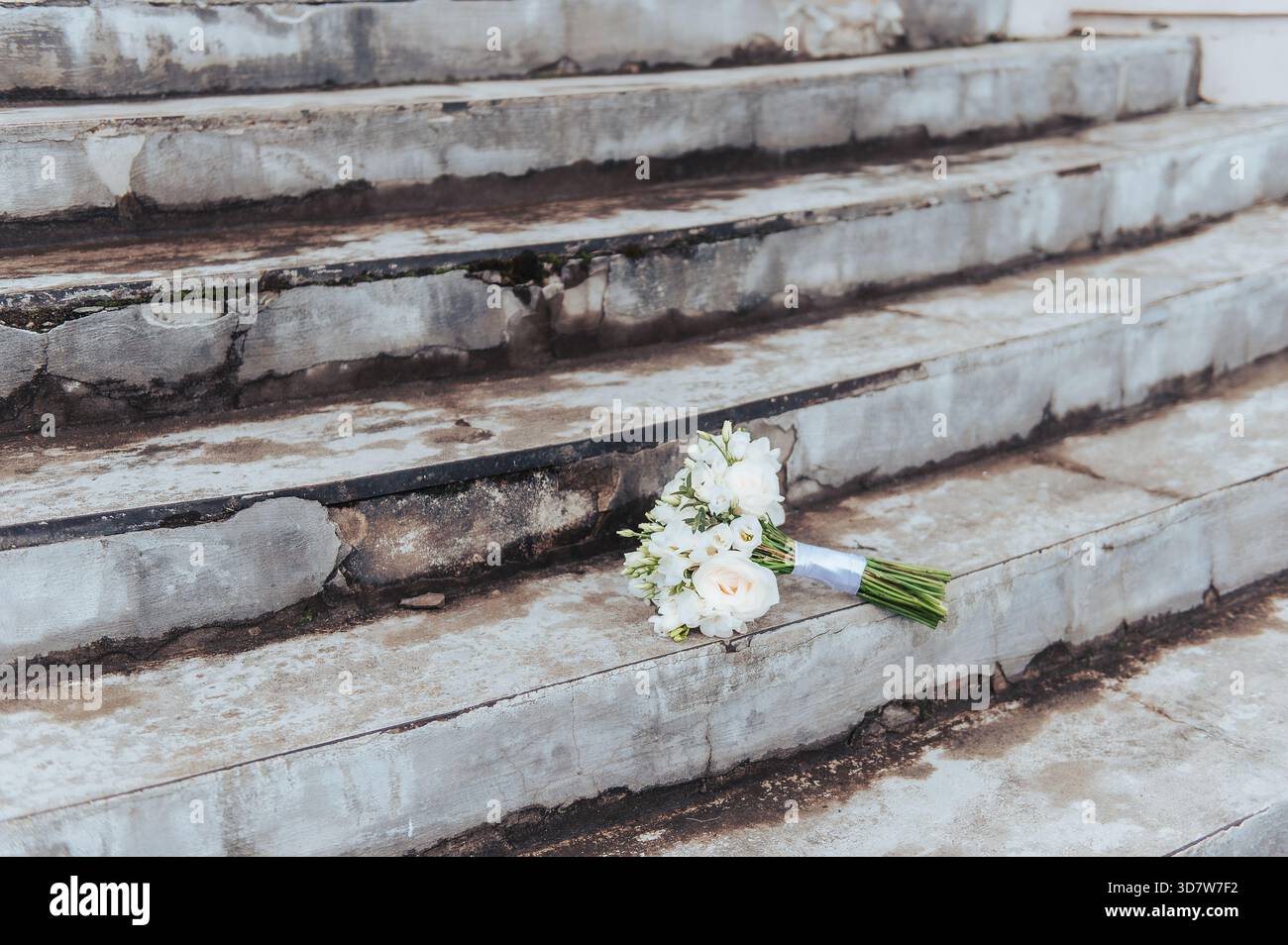 Weißer Hochzeitsstrauß auf abgenutzten Steintreppen, der eine symbolische Hochzeitsszene in Lettland schafft. Stockfoto