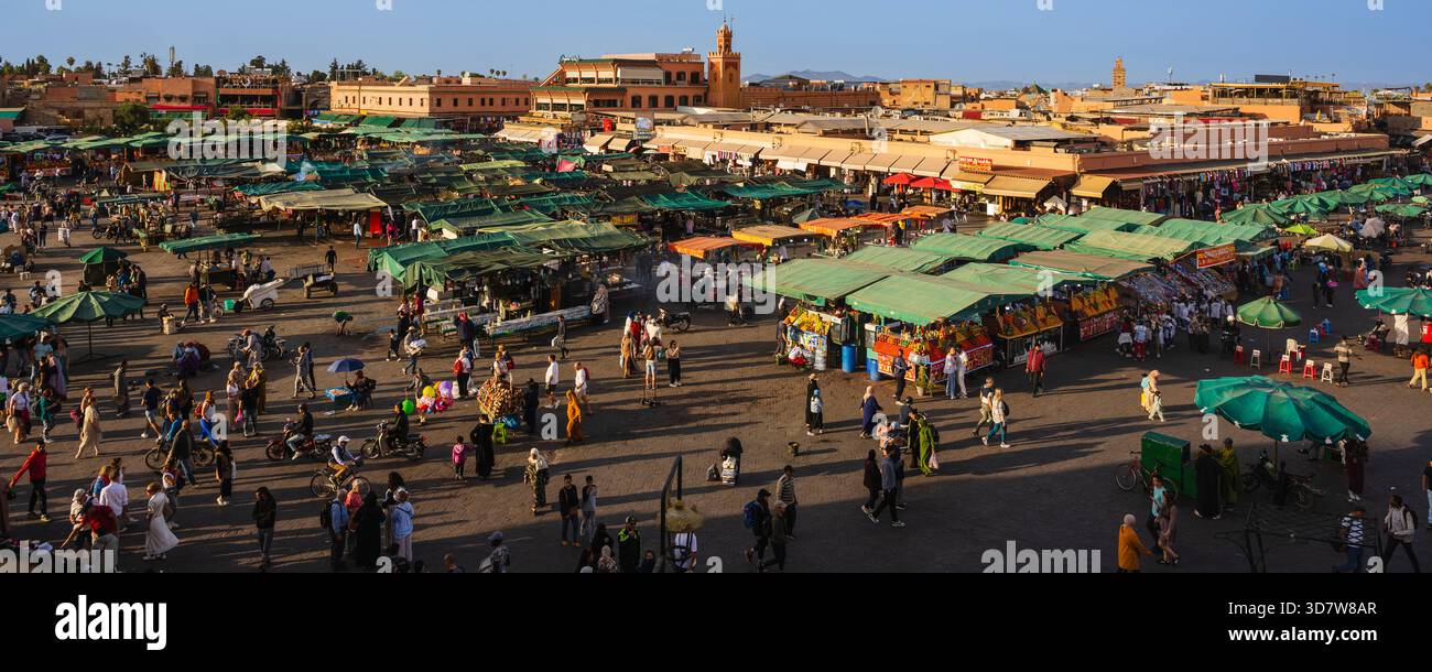 Belebter Markt im Freien mit grünen Ständen, vielfältigen Menschenmengen und historischer Architektur im Hintergrund. Marrakesch, Marokko Stockfoto