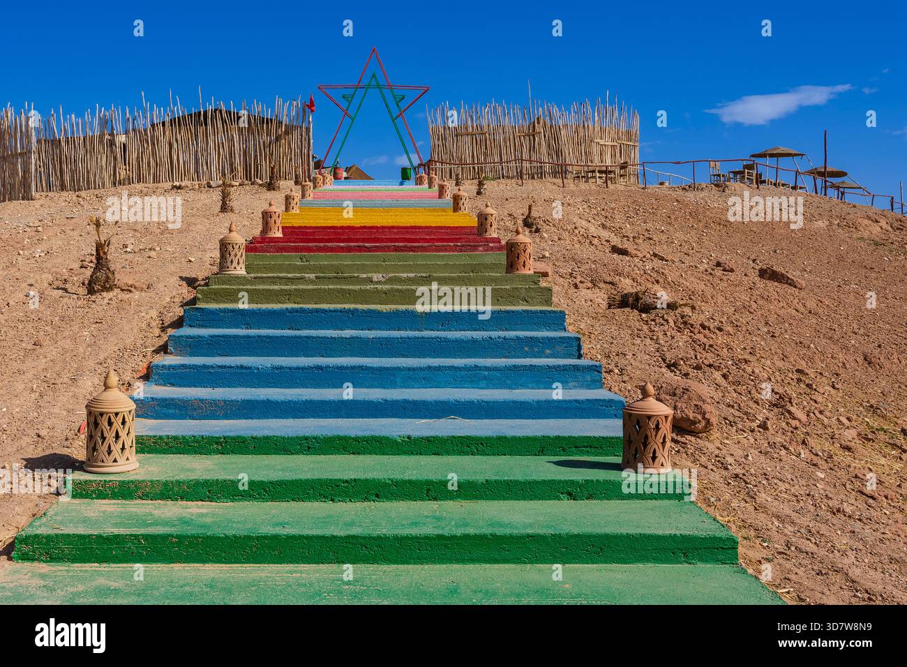 Farbenfrohe Treppen, die zu einem Sternenrahmen führen, umgeben von rustikalen Zäunen in einer Wüstenumgebung. Agafay-Wüste, Marrakesch-Safi, Marokko Stockfoto