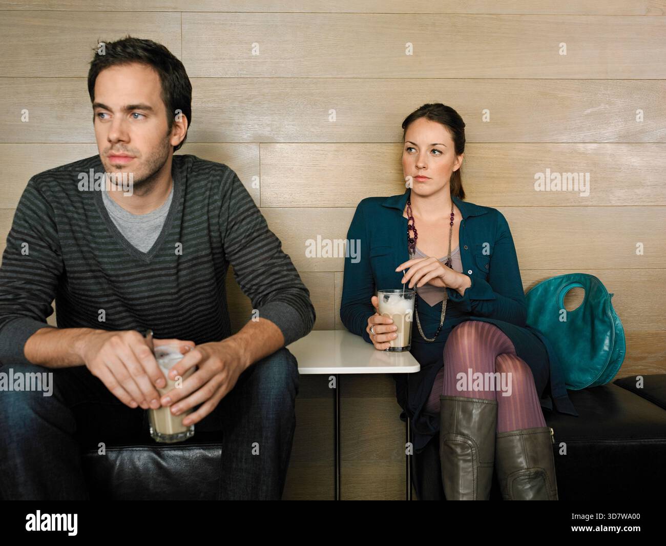 Ein Mann und eine Frau sitzen getrennt in einem Café und halten Drinks. Sie blicken mit neutralen Ausdrücken weg. Deutschland Stockfoto
