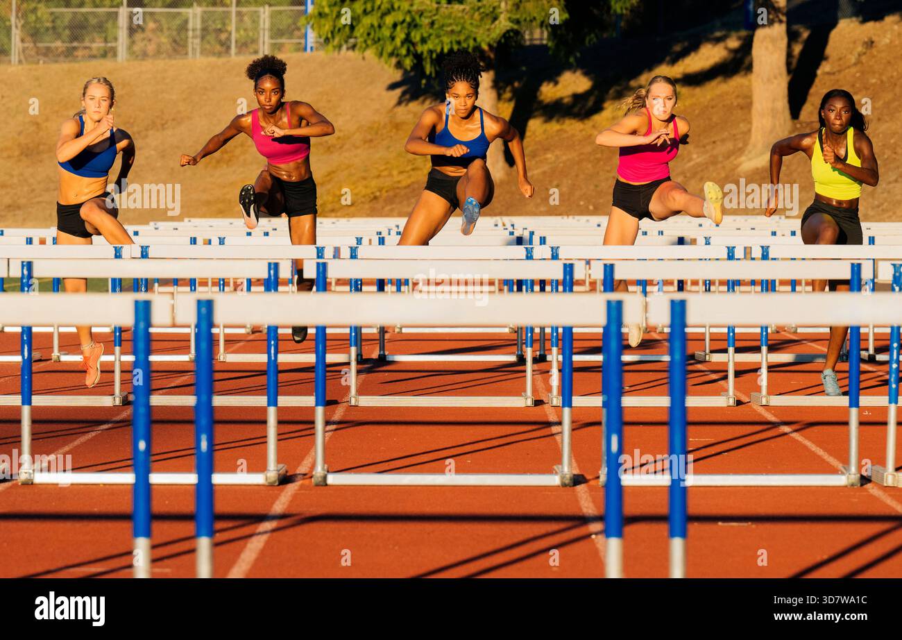 Fünf Frauen sprinten bei warmem Sonnenlicht über Hürden auf einer Outdoor-Strecke. WA, USA Stockfoto