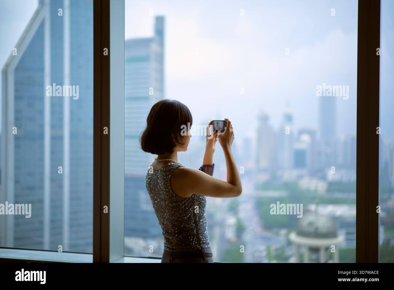 Frau, die ein Foto von einer Skyline der Stadt von einem hohen Aussichtspunkt in der Nähe eines Fensters macht. Shanghai, China Stockfoto