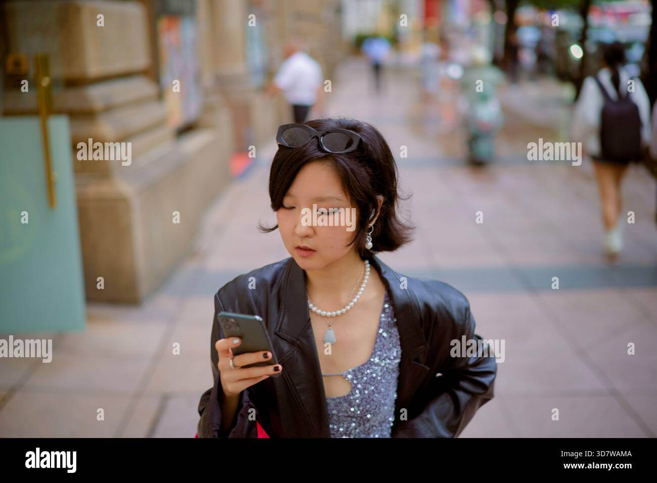 Frau mit kurzen schwarzen Haaren, die auf das Smartphone auf der belebten Stadtstraße schaut. Shanghai, China Stockfoto