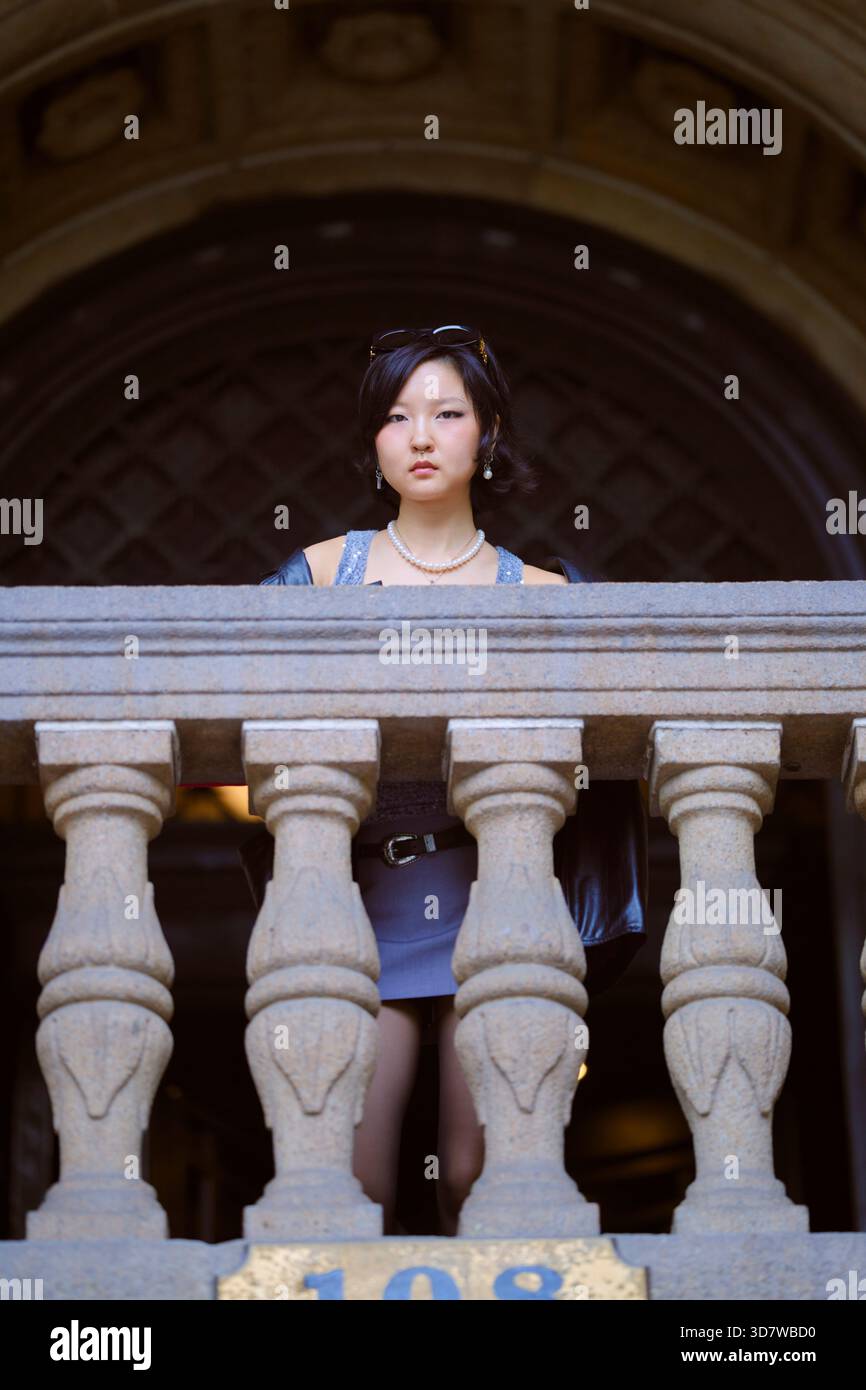 Junge Frau, die hinter einem Steingeländer steht, mit kunstvoller Architektur im Hintergrund. Shanghai, China Stockfoto