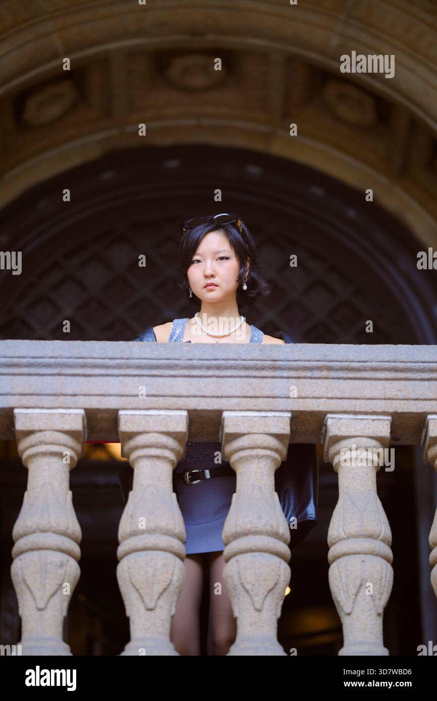Junge Frau, die hinter einem Steingeländer steht, mit kunstvoller Architektur im Hintergrund. Shanghai, China Stockfoto
