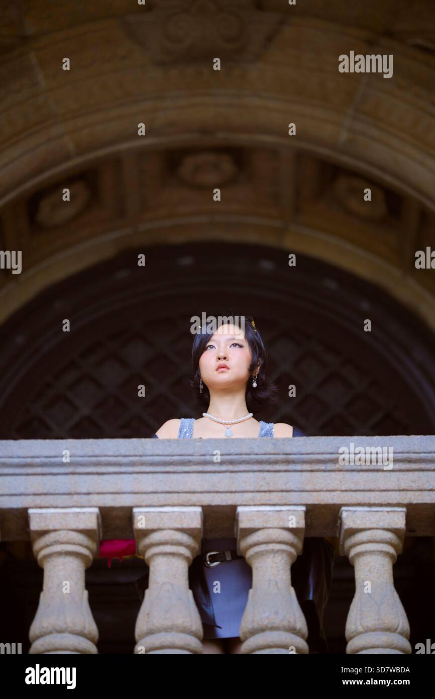 Eine junge Frau mit schwarzen Haaren, die auf einem Steinbalkon unter einem kunstvollen Bogengang steht. Shanghai, China Stockfoto