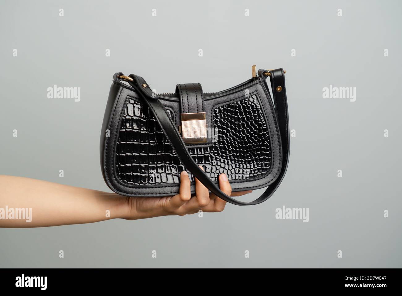 Schwarze Schultertasche Mit Krokodilprägung, Von Hand Auf Einfarbigem Hintergrund Gehalten Stockfoto