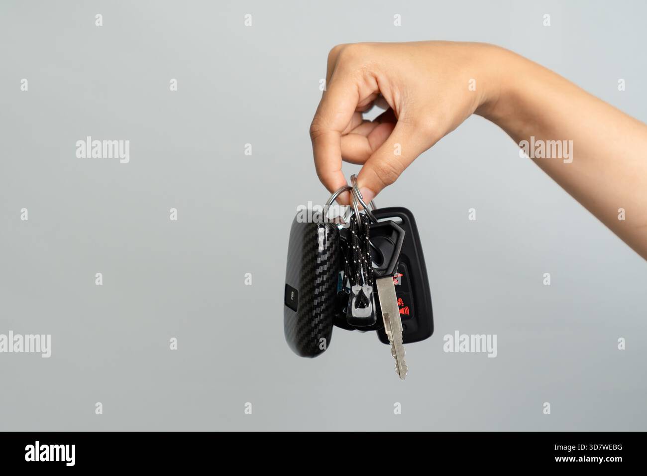 Hand hält Einen Satz moderner Autoschlüssel auf Einer grauen Hintergrundaufnahme im Studio Stockfoto