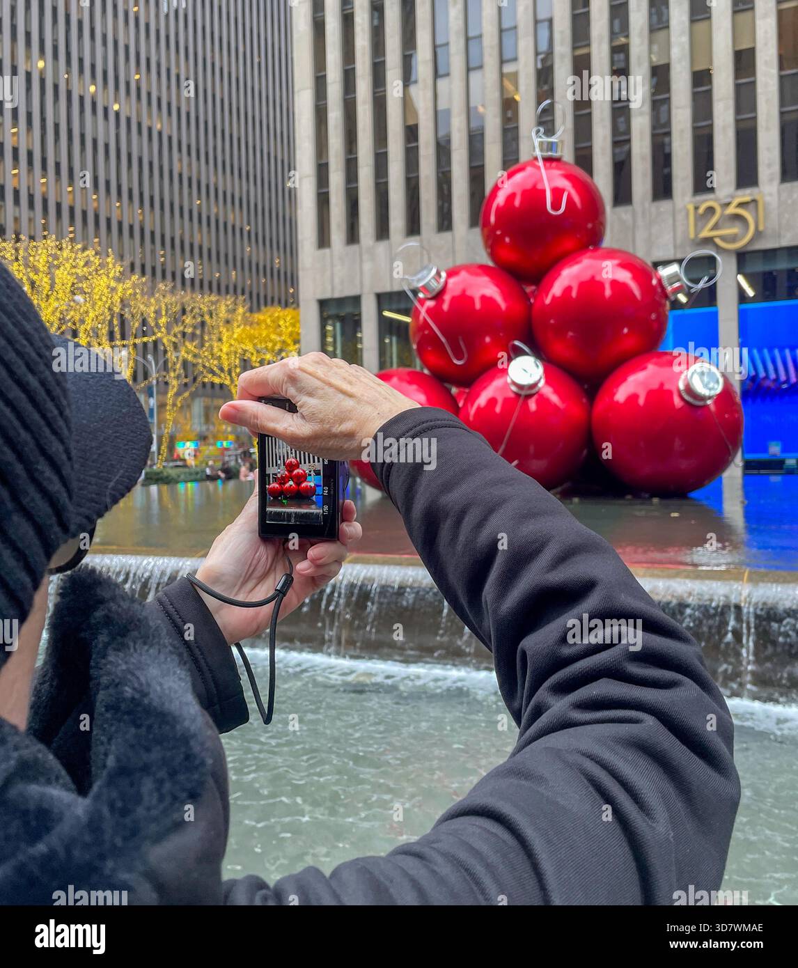 Frau, die ein Foto von Giant Christmas Ornaments macht, Reflecting Pool, 1251 Avenue of the Americas, New York City, USA, 2025 - Smartphone-aufgenommenes Stockfoto