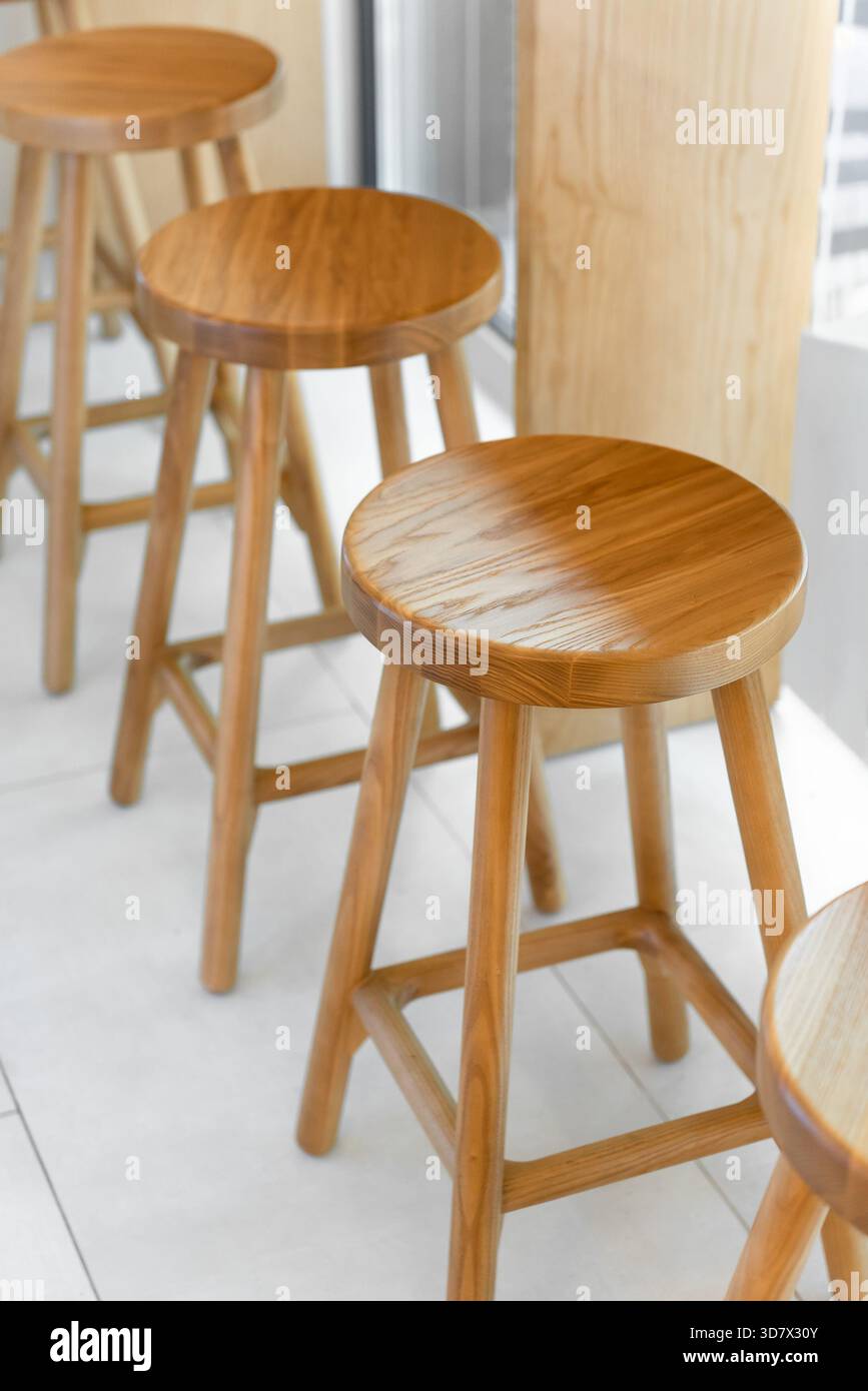 Drei hölzerne Barhocker hintereinander. Runde Holzsitze mit drei natürlichen Holzhölzern in der Nähe eines Fensters. Satte Körnung und Holzstruktur. Stockfoto