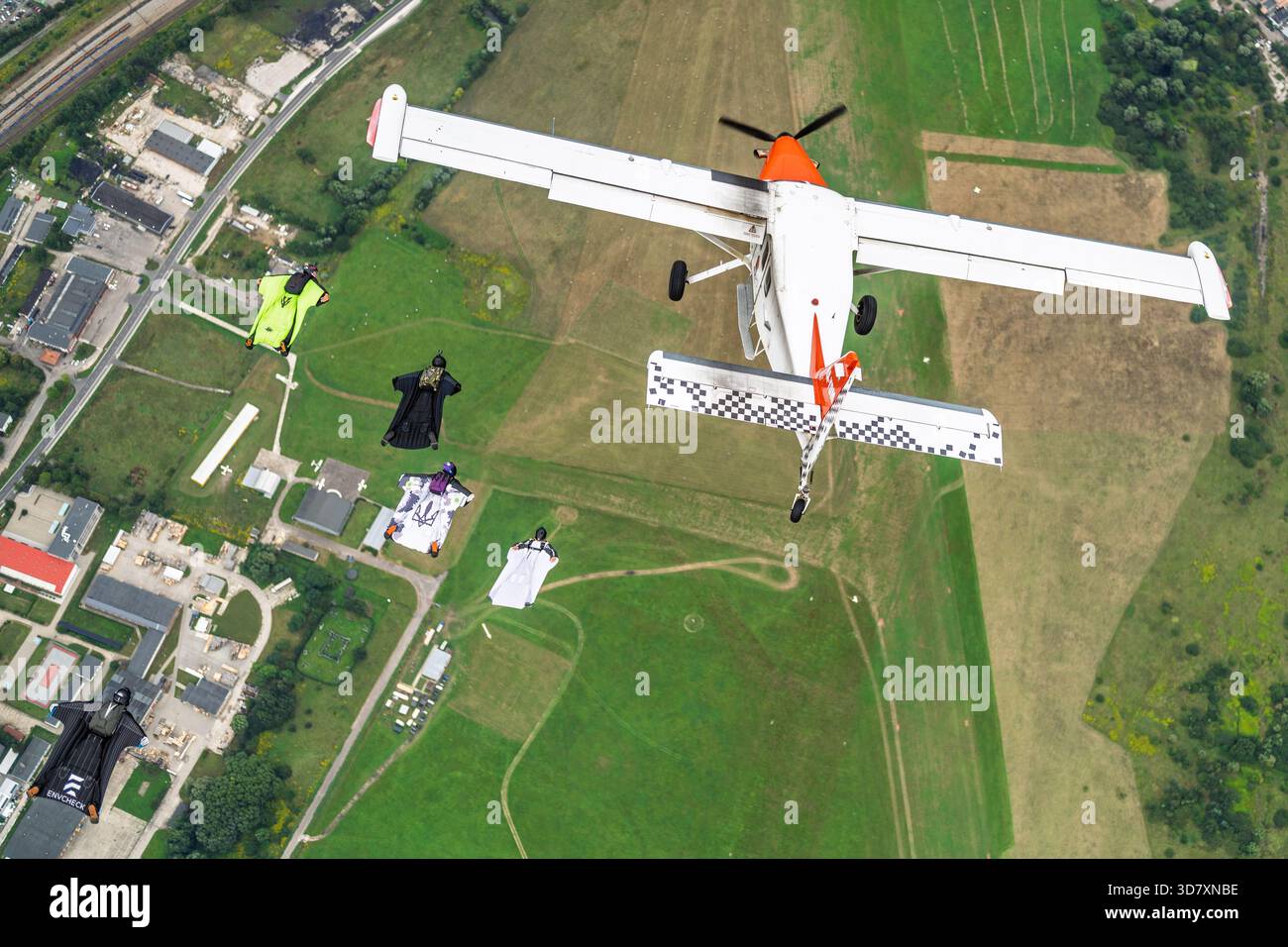 Ein Flugzeug der Technoavia SM-92 Finist STOL fliegt über Farmland, während Wingsuit-Flieger in Formation neben dem freien Fall gleiten. Stockfoto