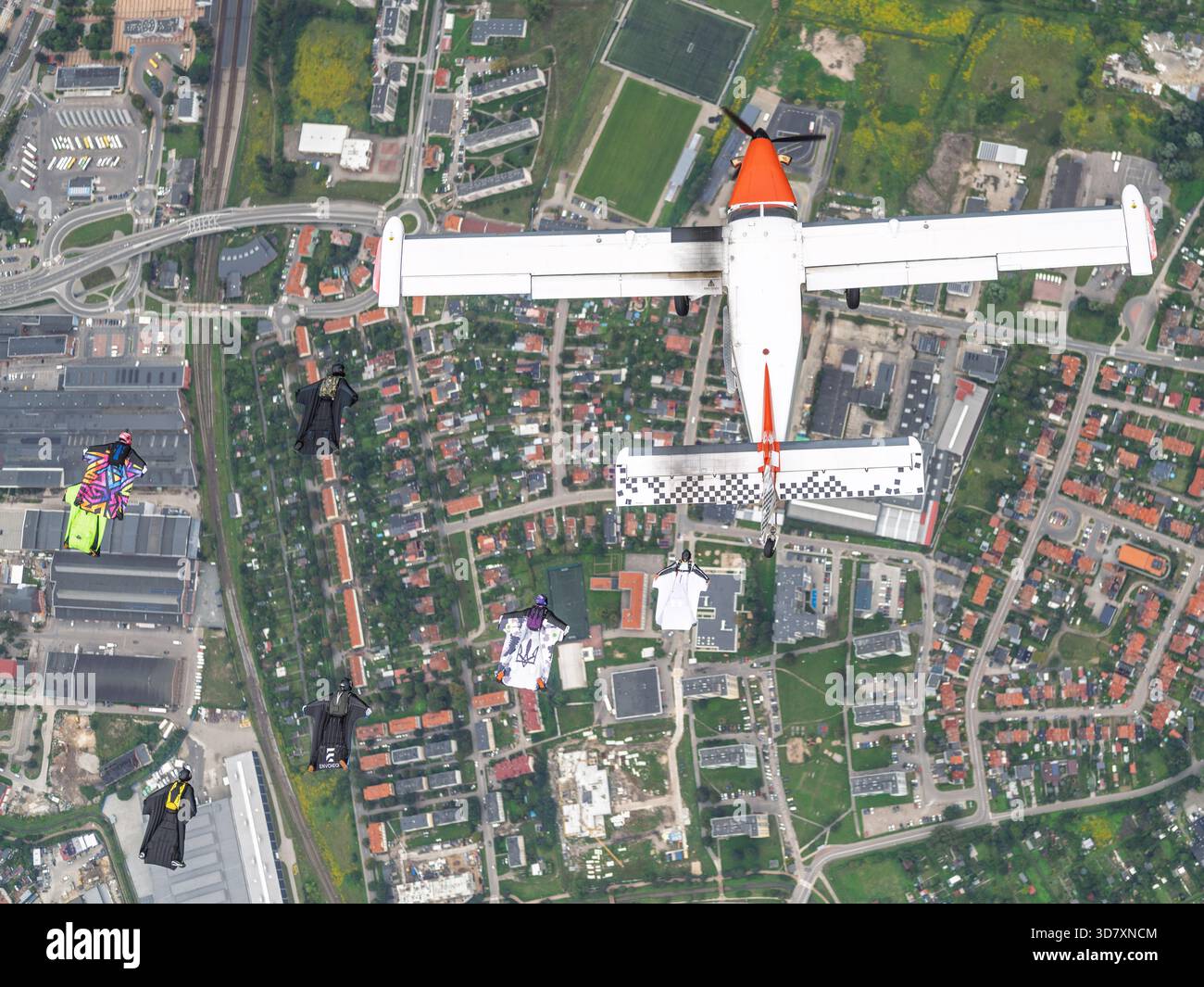 Ein Flugzeug der Technoavia SM-92 Finist STOL fliegt über Farmland, während Wingsuit-Flieger in Formation neben dem freien Fall gleiten. Stockfoto