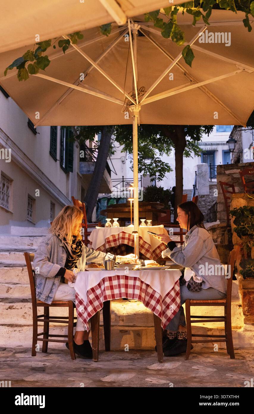 Zwei Freundinnen sitzen abends draußen in einem Restaurant und essen und trinken; Plaka, Athen, Griechenland, Europa Stockfoto