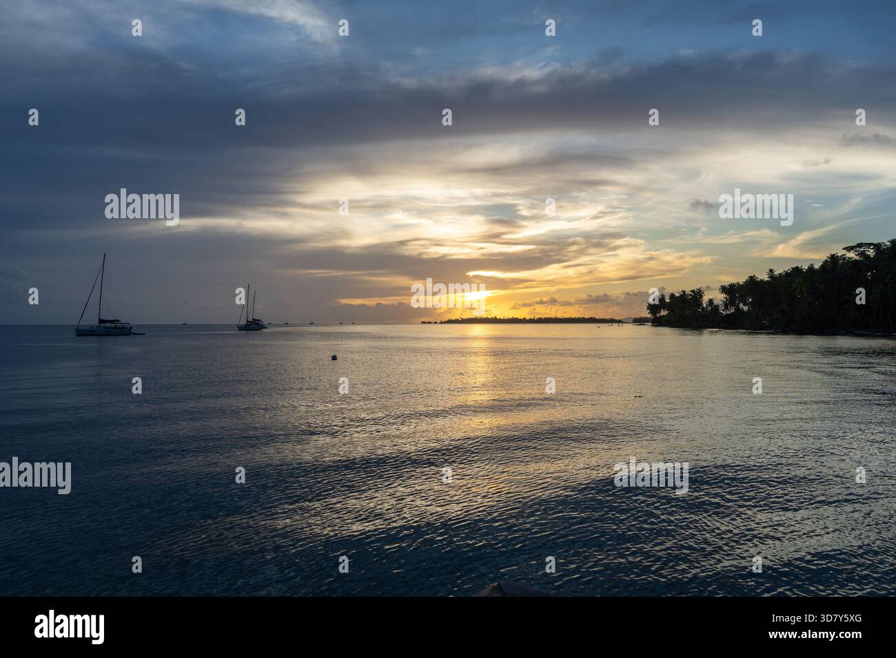 Ein wunderschöner Sonnenuntergang über der Insel Tahaa in Französisch-Polynesien, mit ruhigem Wasser und Segelbooten, die eine ruhige Atmosphäre schaffen Stockfoto