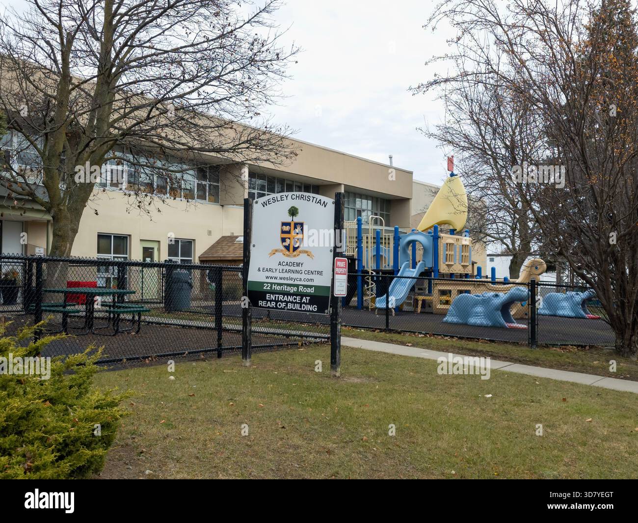 Äußere der Wesley Christian Academy mit Spielplatz, Fischrutsche, schwarzem Zaun und grasbewachsenen Bäumen in Ontario - Smartphone-aufgenommenes Stockfoto