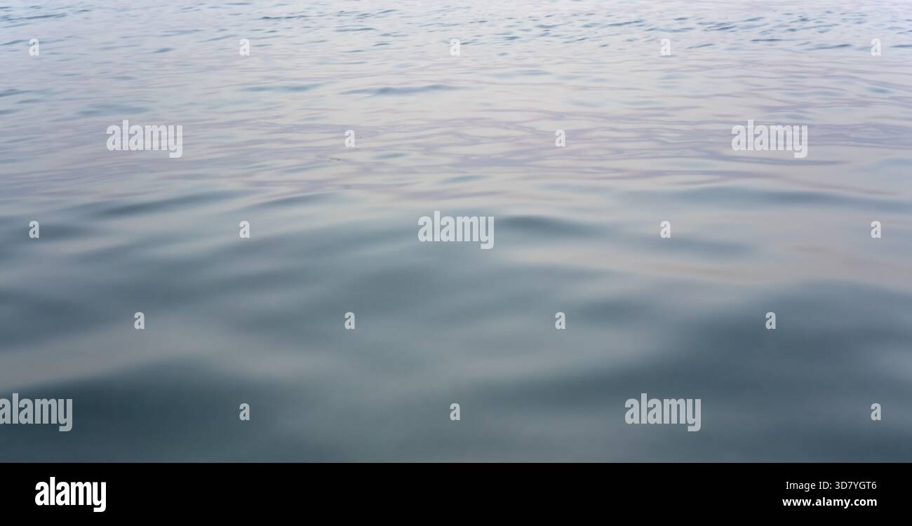 Ruhige Meereswasseroberfläche nach Sonnenuntergang, nur kleine Wellen - abstrakter Meereshintergrund Stockfoto