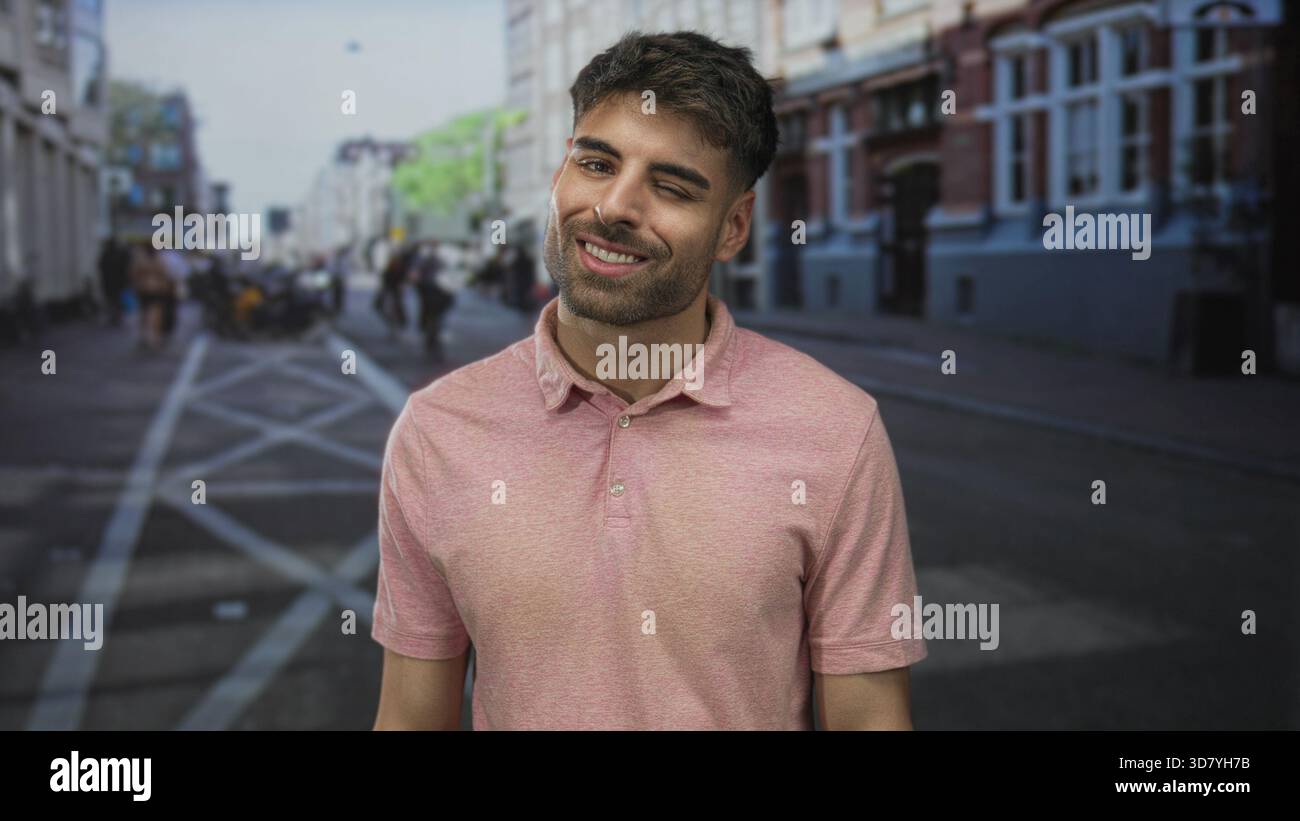 Mann lächelt in einem rosa Polo auf einer überfüllten Stadtstraße mit verschwommenen Fußgängern und Gebäuden im Blick; Glück. Stockfoto