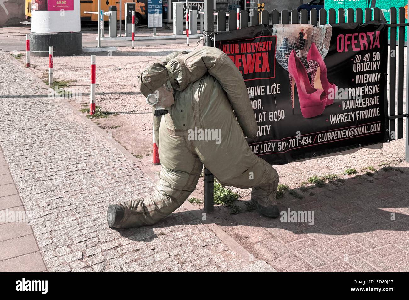 Schrullige Straßenszene mit einer Schaufensterpuppe in einem Gefahrenanzug und einer Gasmaske, die sich an einer Stange neben einem Clubbbanner stützt. Stockfoto