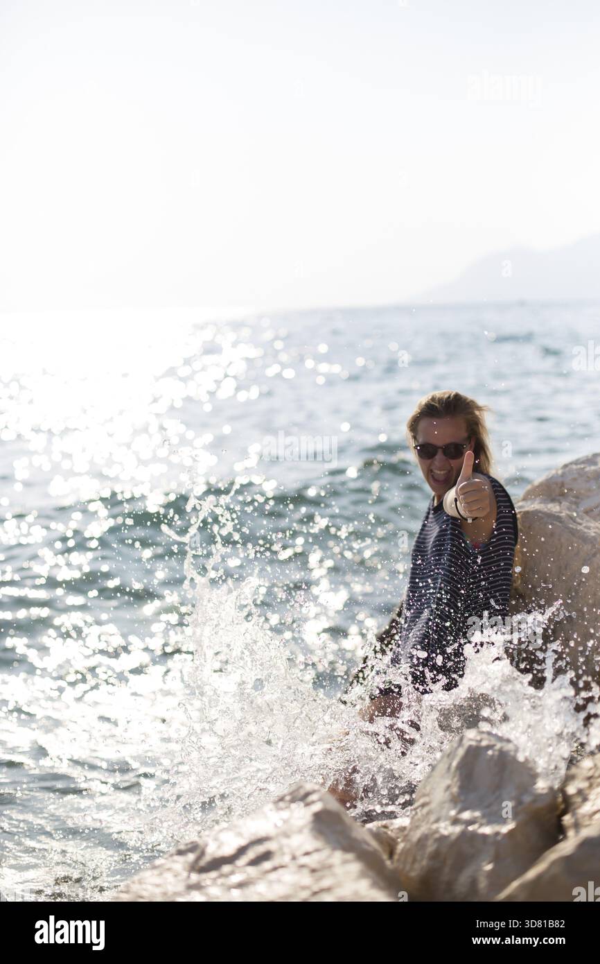 Schöne Frau auf einem Stein sitzend und planschen im Meer Stockfoto