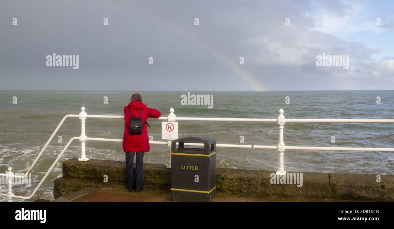 Bridlington, England, 10. August: Dame in Rot, die auf einen Regenbogen blickt, während stürmisches Wetter über die Küste stürmt 10. August: 2014 Bridlington, England Stockfoto
