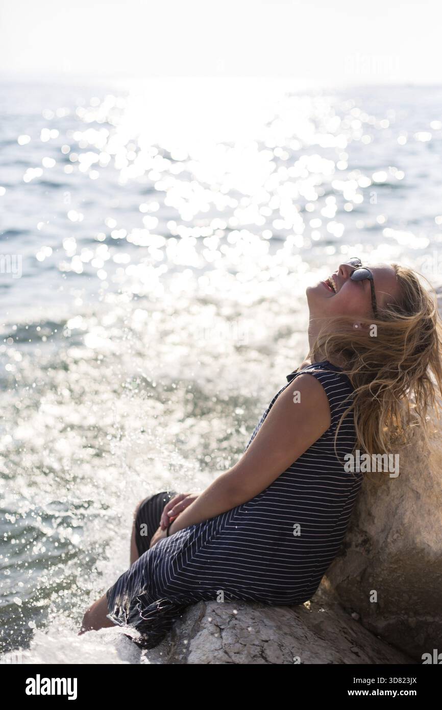 Schöne Frau auf einem Stein sitzend und planschen im Meer Stockfoto