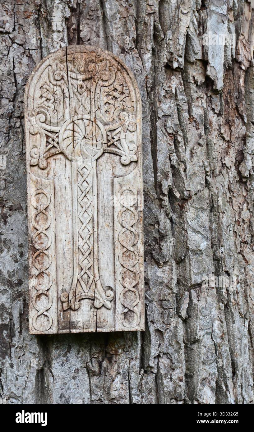 Armenischer Khachkar aus Holz mit traditionellen Schnitzereien, die auf einem Baumstamm in einem Wald montiert sind Stockfoto