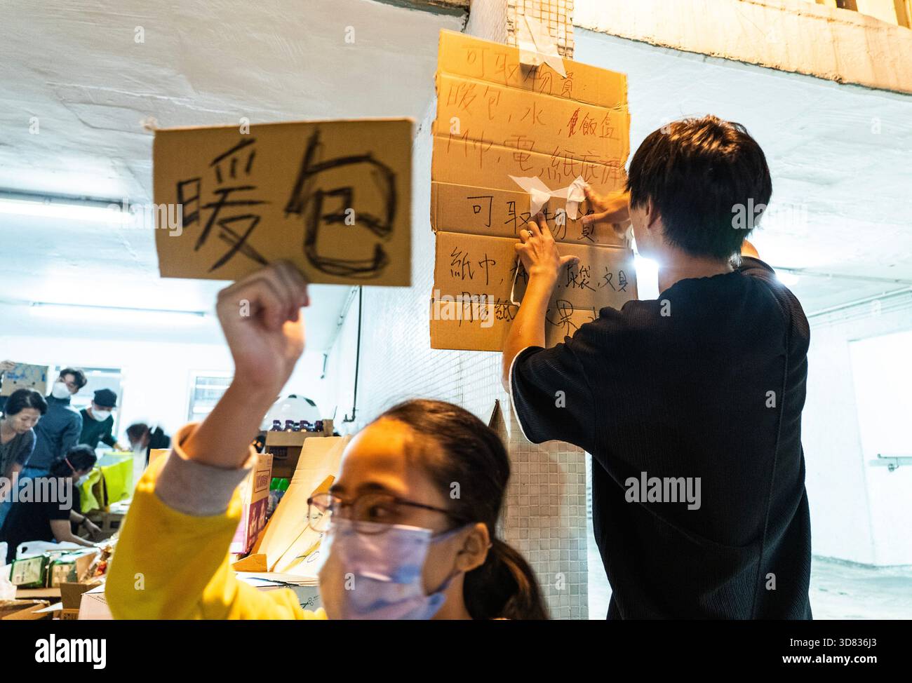 Teenager stellen Schilder für Materialvorräte auf. Hongkong, China, 27. November 2025. Teenager beteiligen sich am Abend des 27. November 2025 an der Bereitstellung von heißem Wasser, Warmwasserpackungen und anderen Vorräten für die Bewohner in der Nähe des Brandortes in Hung Fuk Court, Tai Po, Hongkong. Quelle: Hou Yu/China News Service/Alamy Live News Stockfoto