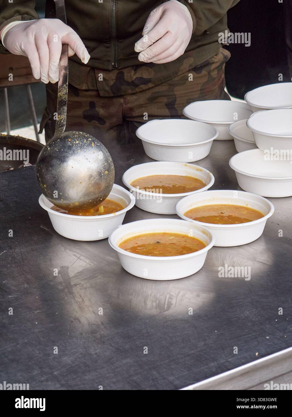 Volunteer Serving Hot Soup into Disposable Bowls in a Military Camp Stockfoto