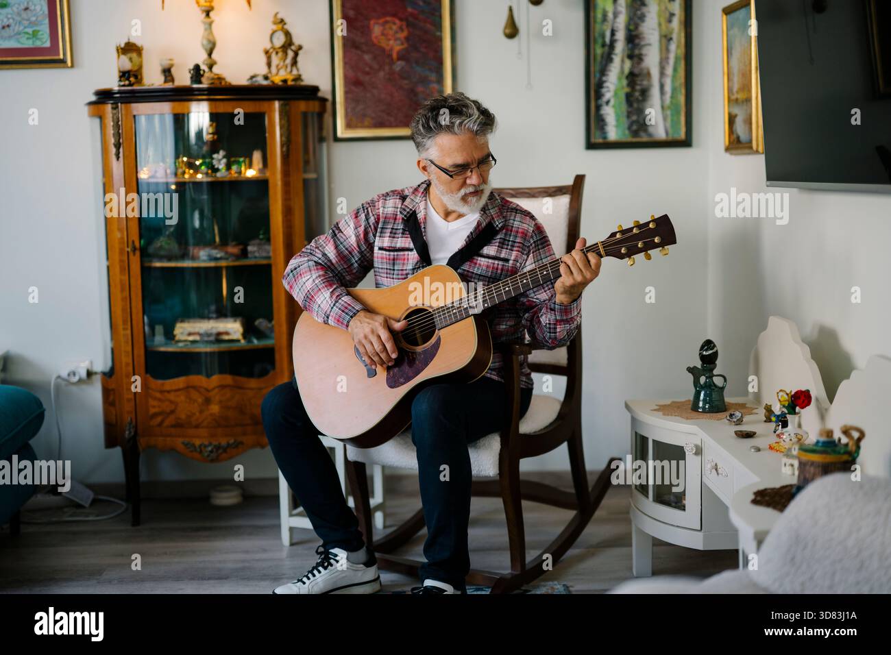 Senior-Mann spielt Akustikgitarre in einem gemütlichen Wohnzimmer Stockfoto