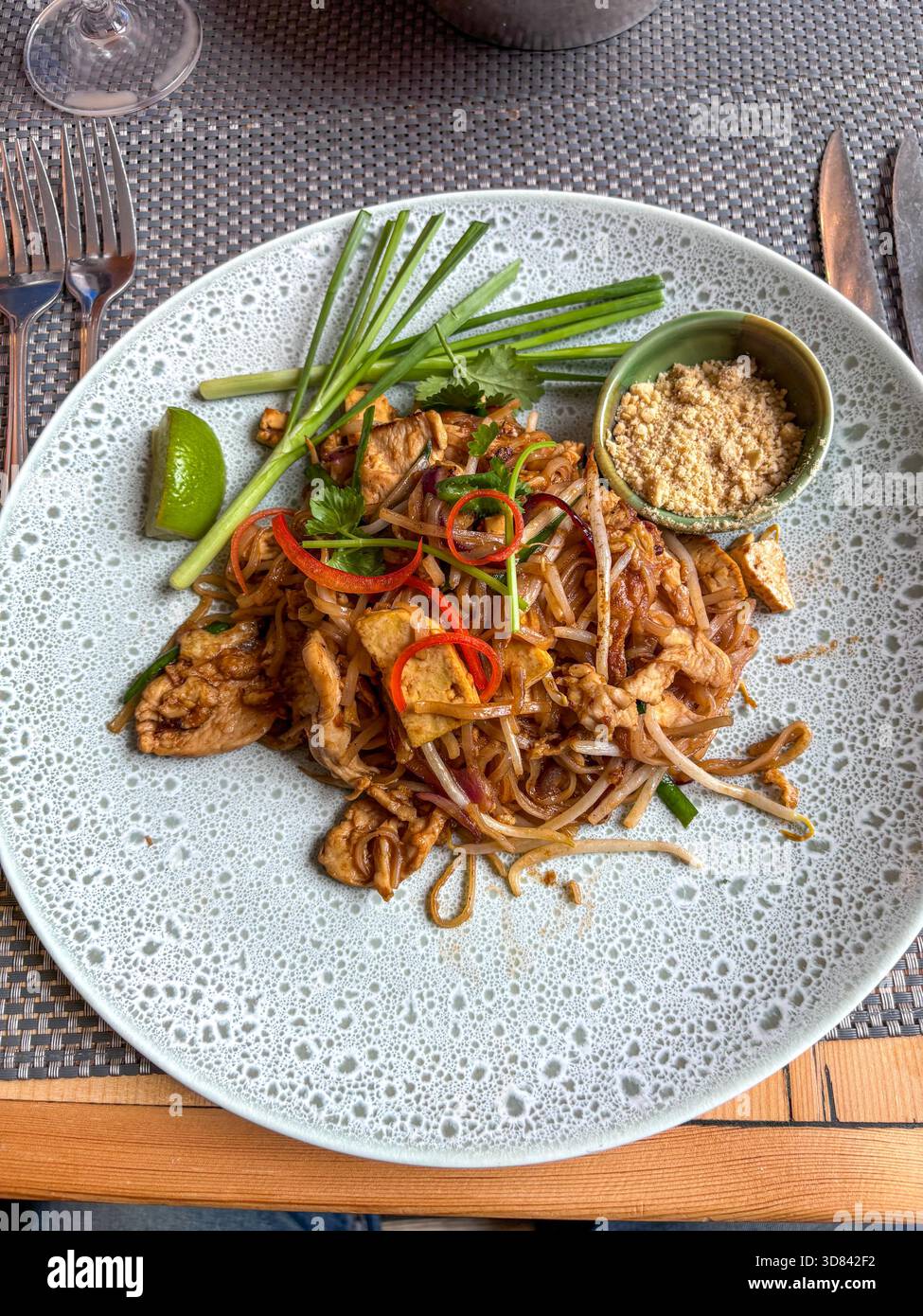 Klassisches Pad Thai Gericht mit Hühnchen, Nudeln, Bohnensprossen, Erdnüssen und Limette auf einem modernen Restauranttteller Stockfoto