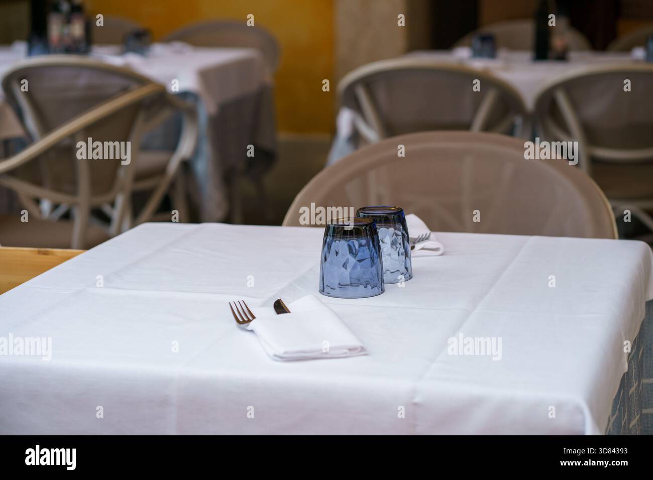 Ordentlich angeordnete Esstische im Freien mit weißen Tüchern, umgedrehten Gläsern und gefalteten Servietten mit Besteck. Stockfoto