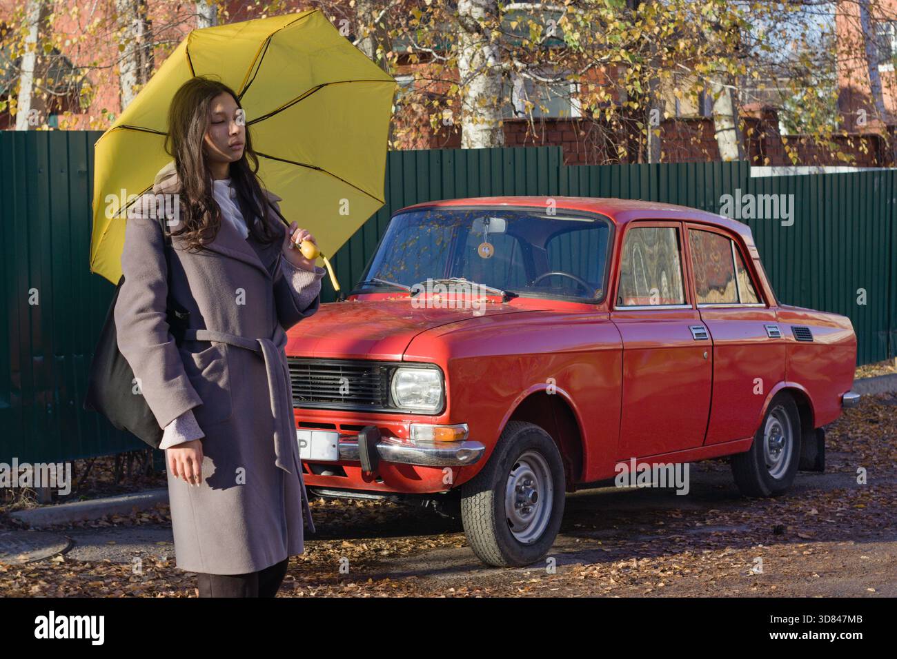 Eine junge Indianerin schlendert an einem roten Oldtimer vorbei und hält einen gelben Regenschirm Stockfoto