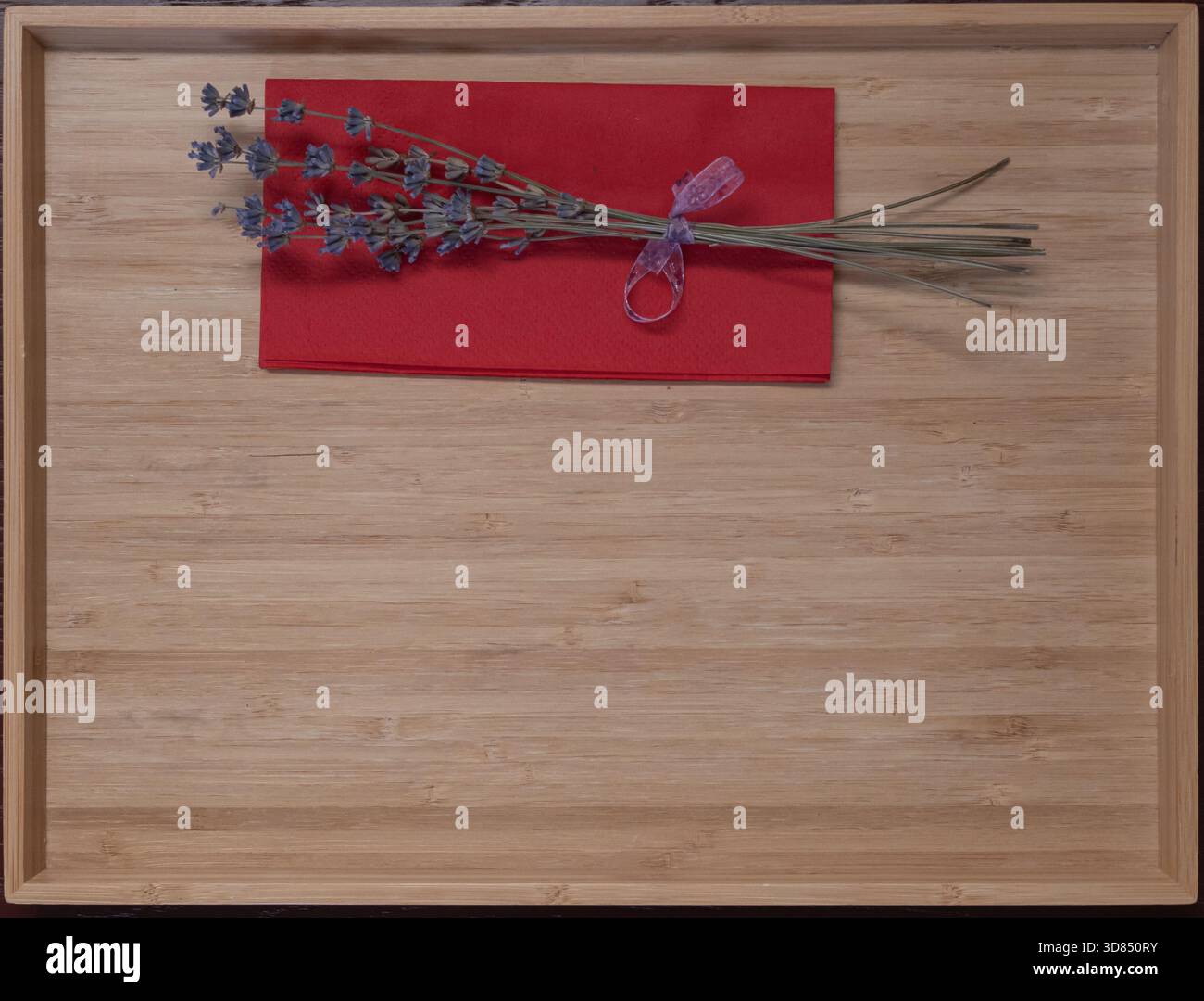 Getrocknetes Lavendelstrauß, gebunden mit Band, auf einer roten Serviette auf einem Holztablett, rustikale, minimalistische Einrichtung für Dekor- und Aromatherapie-Themen. Stockfoto