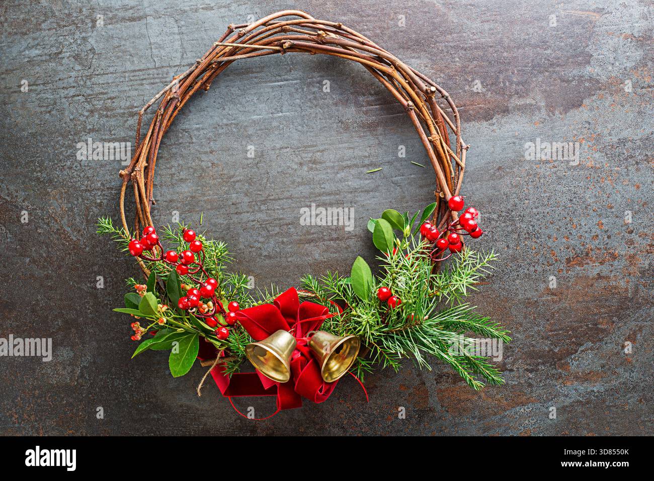 Weihnachtskranz aus natürlichen Zweigen, rote stechpalmenbeeren mit roter Schleife und goldener Glocke. Stockfoto