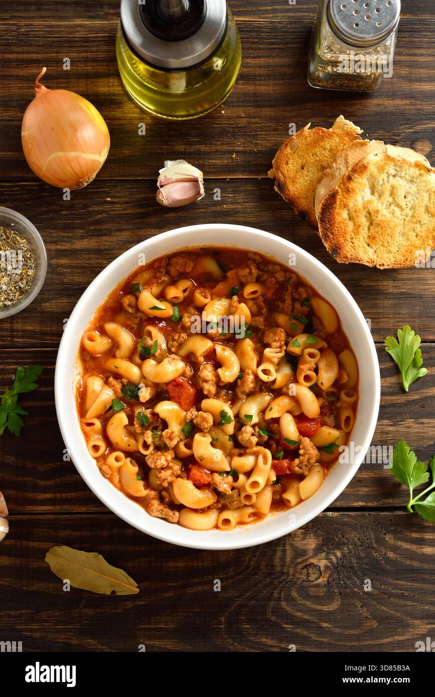 Amerikanisches Gulasch, Gericht mit gemahlenem Rindfleisch und Ellenbogenmakkaroni in Tomatensauce in einer Schüssel auf Holztisch. Draufsicht, flach Stockfoto