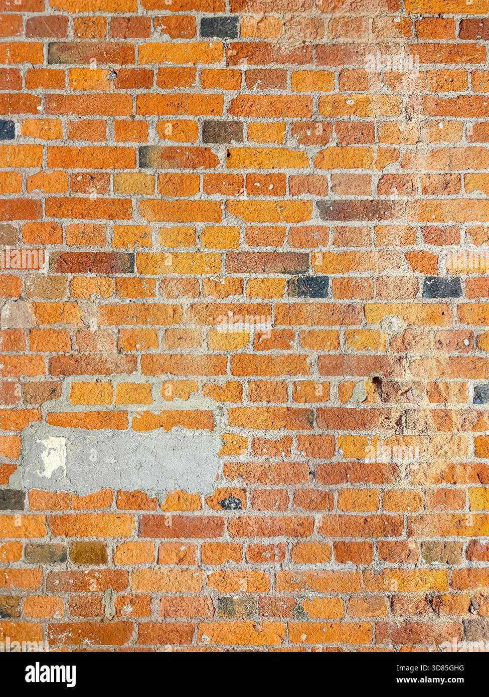 Verwitterte rote und orangene Ziegelwand mit sichtbarem Mörtel und Putzflecken, die Anzeichen von Alter und Reparatur zeigen - Smartphone-aufgenommenes Stockfoto