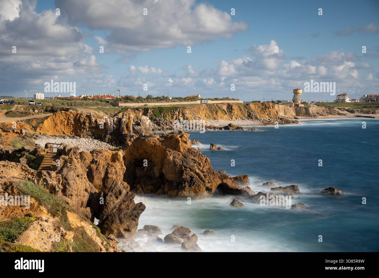 Die felsige Küste von Peniche mit Wellen, die unter hellem Himmel gegen die Klippen krachen, zeigt die zerklüftete Atlantiklandschaft im Westen Portugals. Stockfoto
