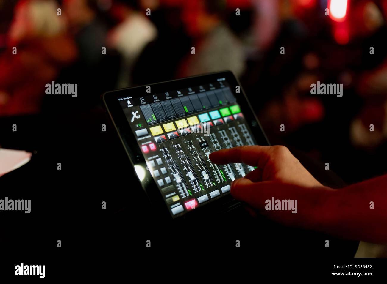 Audio-Mixer auf Tablet-Basis in einem belebten Veranstaltungsraum mit sanfter roter Beleuchtung, die die technische Seite der Live-Event-Produktion, des Soundmanagements und veranschaulicht Stockfoto