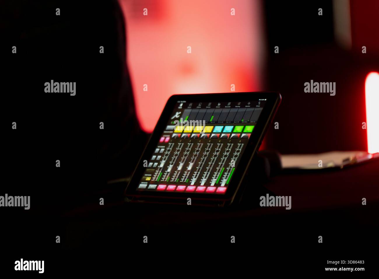 Tablet-basierte Mischkonsole mit mehreren Audiokanälen und Messgeräten, die das technische Setup hinter zeitgenössischer Eventproduktion und Livestream erfasst Stockfoto