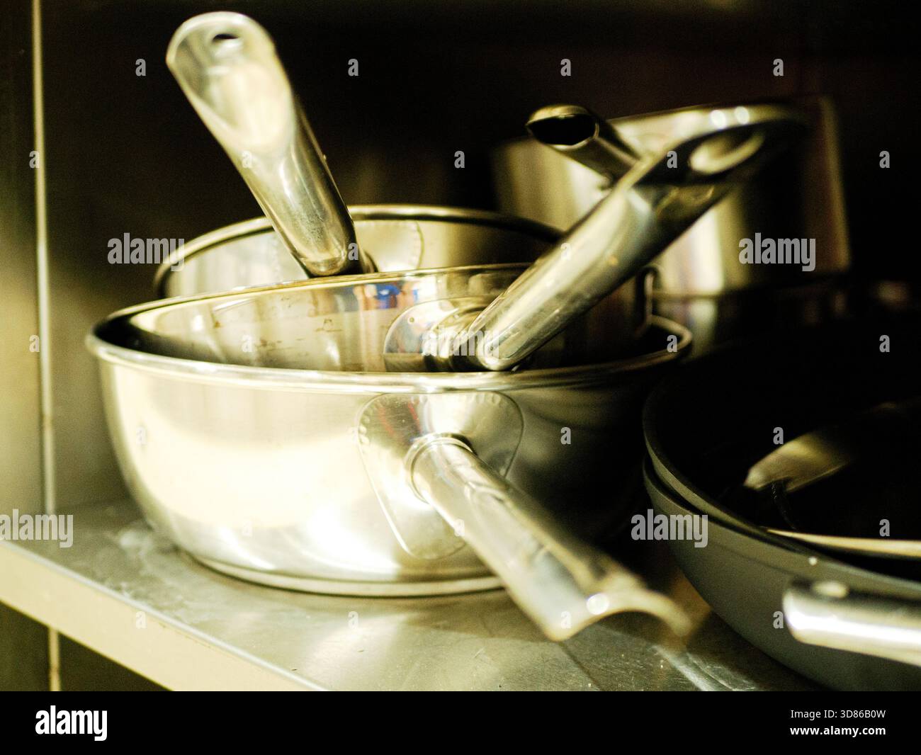 Töpfe aus Edelstahl und Kochgeschirr mit Griff ordentlich auf Metallregal in der professionellen Küche angeordnet. Hochwertiges Foto Töpfe aus Edelstahl Stockfoto
