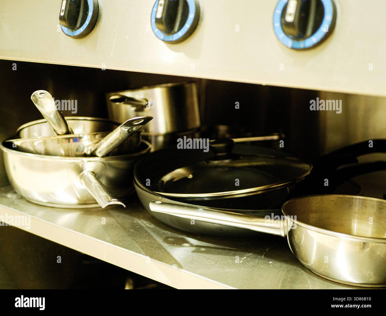 Metallregal mit Töpfen, Pfannen und Küchenutensilien aus Edelstahl unter dem industriellen Restaurantofen in der professionellen Geschäftsküche Stockfoto