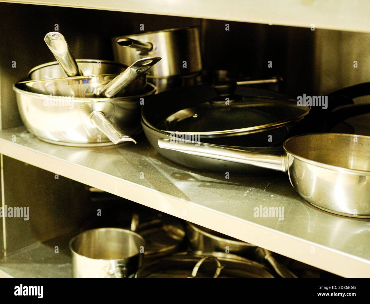 Kochgeschirr, Pfannen und Utensilien aus Edelstahl werden auf einem Küchenregal aus Metall in einem professionellen Restaurant mit organisierter kommerzieller Küche gelagert Stockfoto