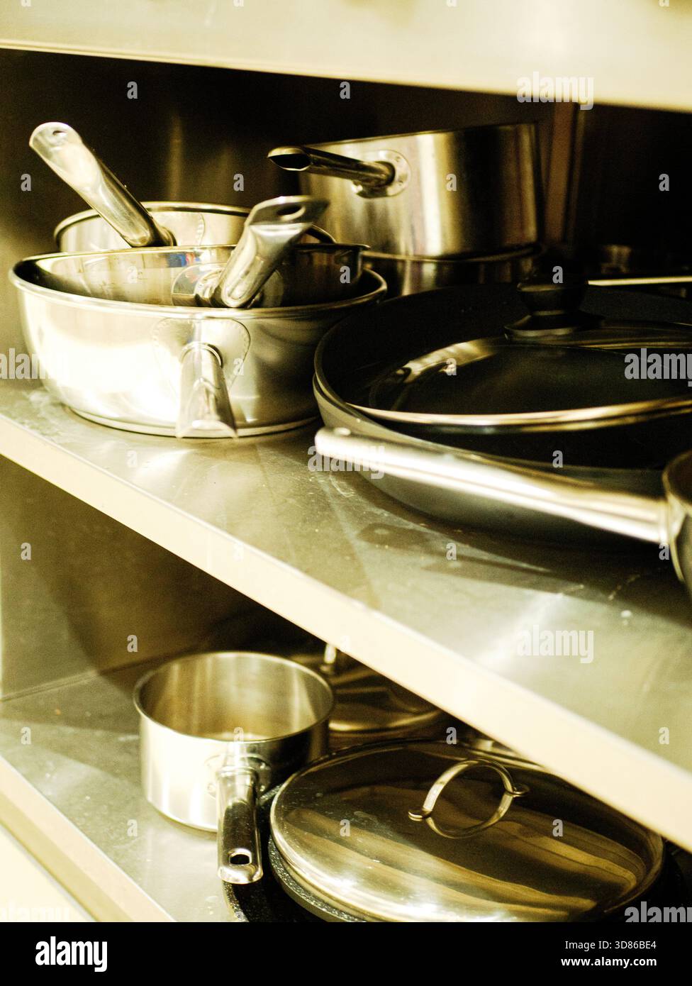 Kochgeschirr und Utensilien aus Edelstahl werden auf Metallregalen in der professionellen Küche des Restaurants gelagert. Hochwertiges Foto Töpfe, Pfannen aus Edelstahl Stockfoto
