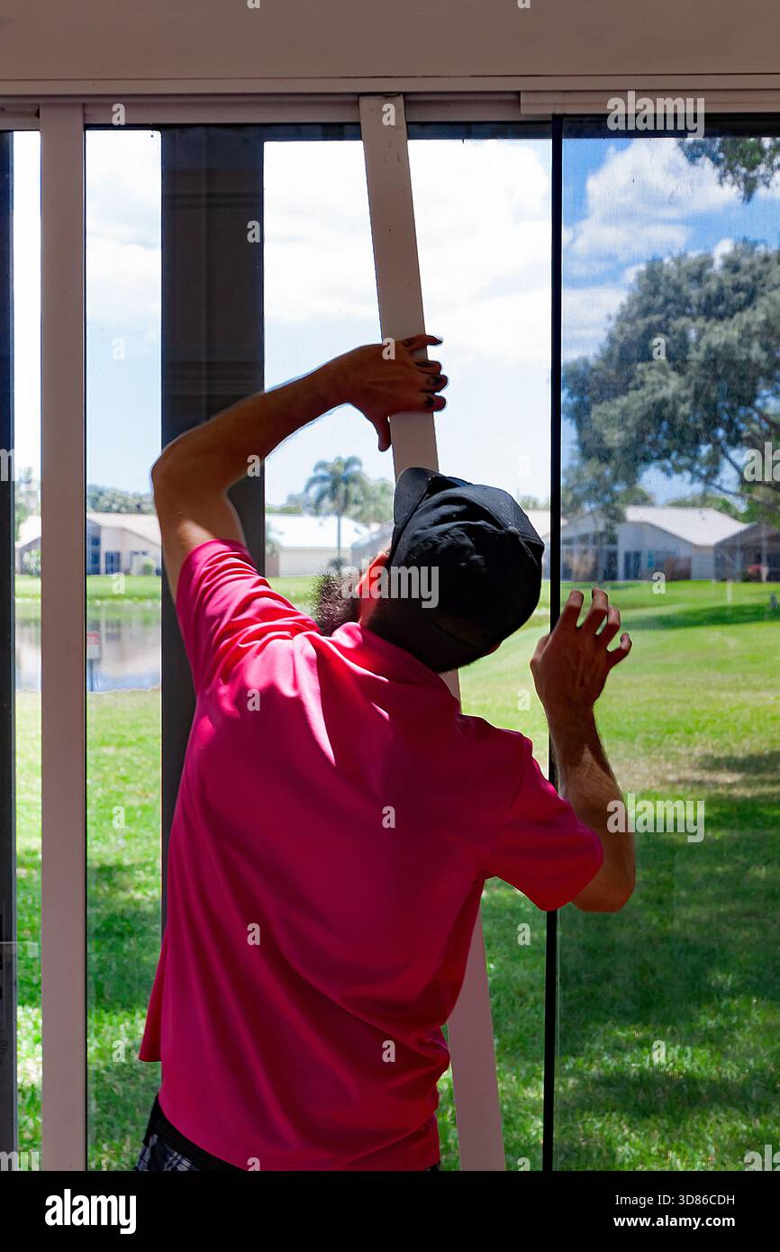 Reparaturarbeiter, der Glasschiebetüren und Gittertüren aufgrund abgenutzter Rollen und Schienen im Innenhof eines Hauses befestigt, Stockfoto