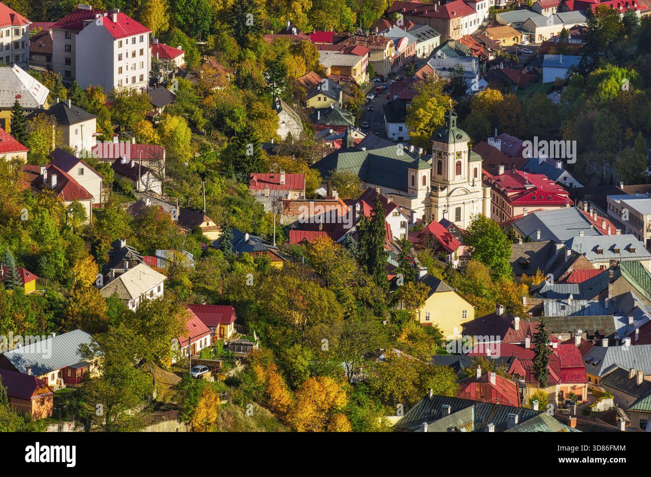 Blick aus der Vogelperspektive auf farbenfrohe Dächer und Bäume, die um eine Kirche herum liegen und einen lebendigen Wandteppich aus herbstlichen Tönen schaffen, Banska Stiavnica, Banska Bystrica Regi Stockfoto