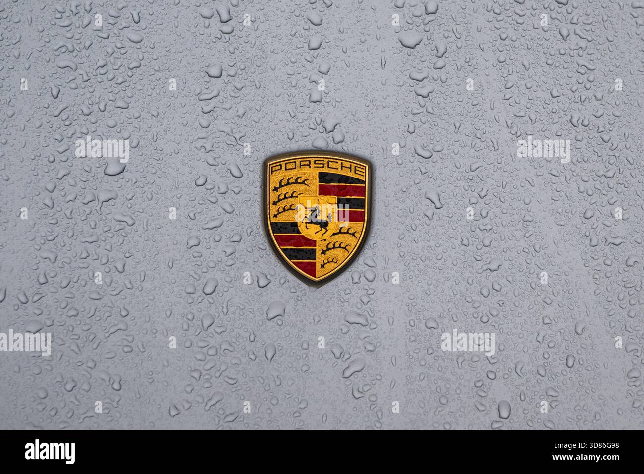 Porsche-Logo auf der regenbedeckten Motorhaube eines Porsche Taycan GTS. Stockfoto